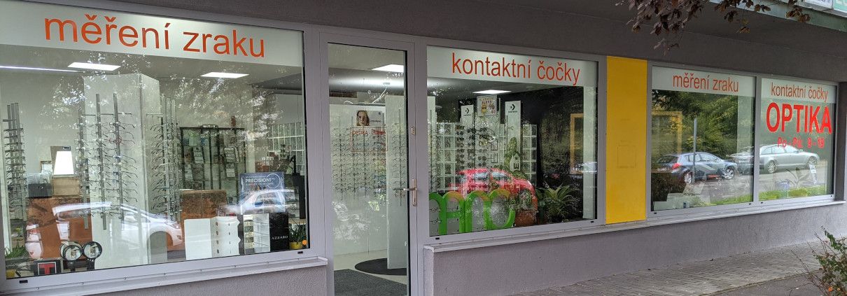 Výloha Optiky Lužiny s oranžovými nápisy měření zraku a kontaktní čočky